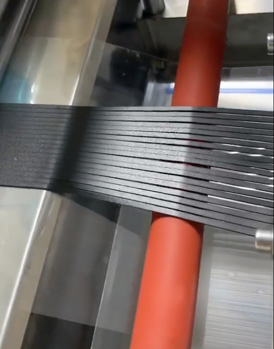 Narrow die-cut black strips running over a red roller inside a converting machine