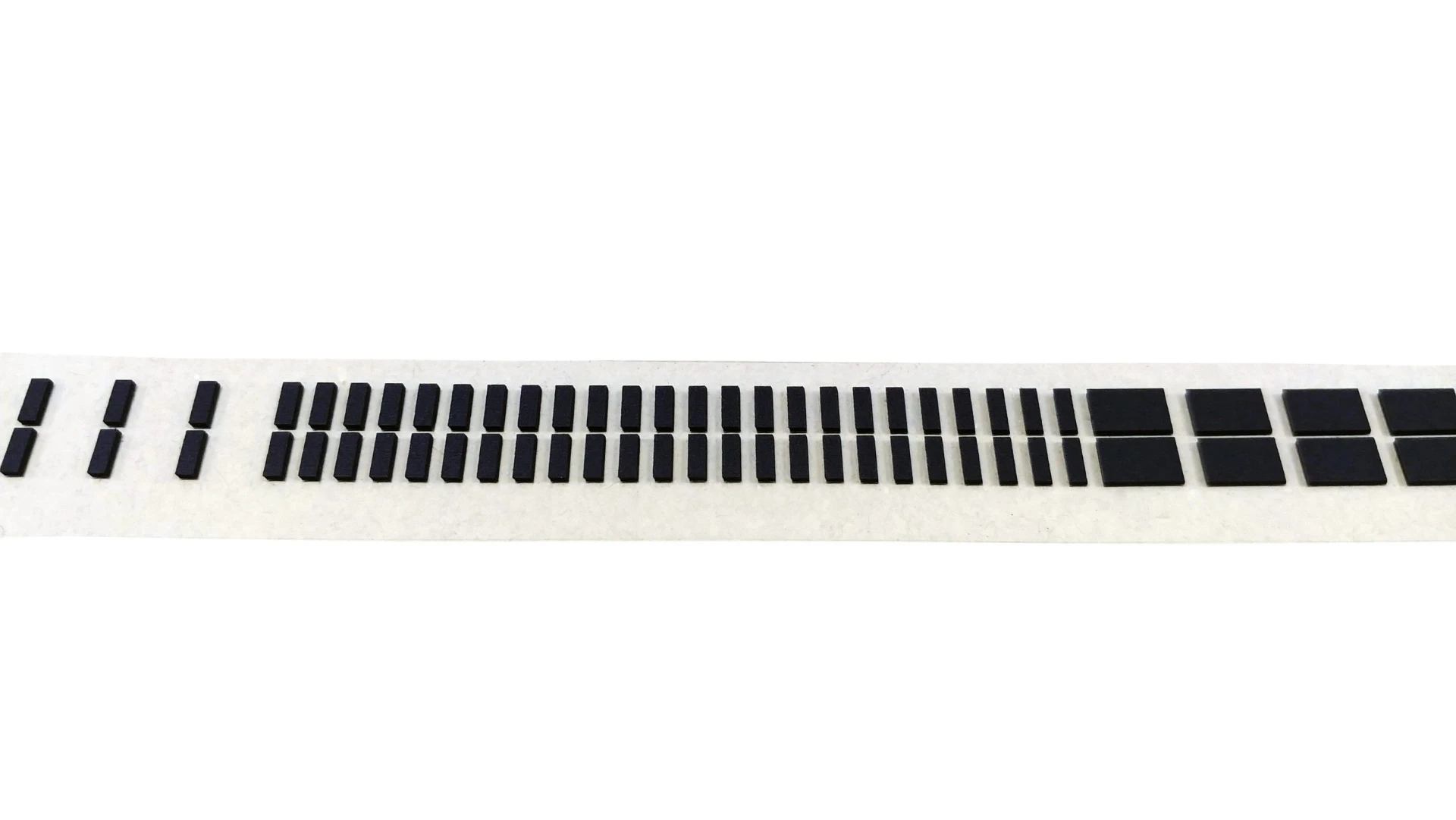 Continuous carrier strip of small black die-cut foam parts in graduated sizes